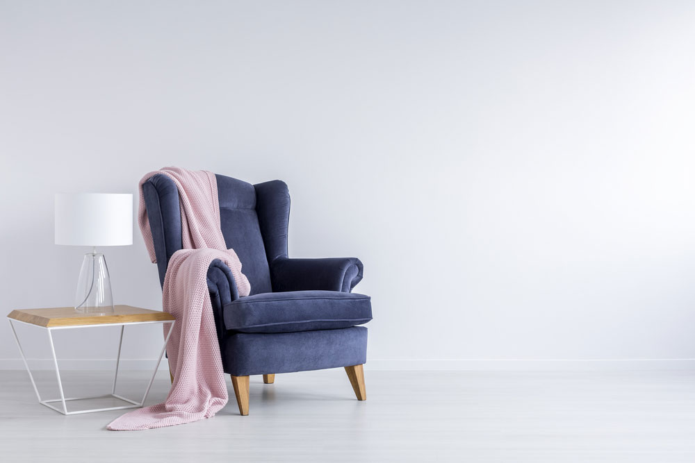 Blue chair with pink blanket on it against white wall