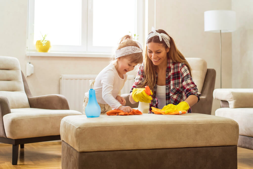 A mother and daughter are spring-cleaning in a light and airy living room. 