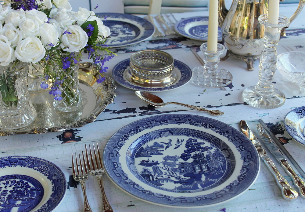 A styled table is set with blue willow dish ware and gold flat fare