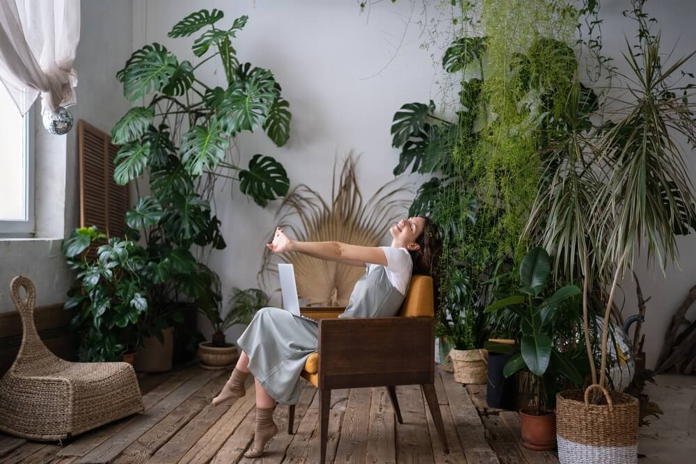 A woman sits in a chair in room with lots of house plants 