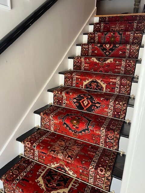 A vintage rug is used as a runner on a set of wooden stairs